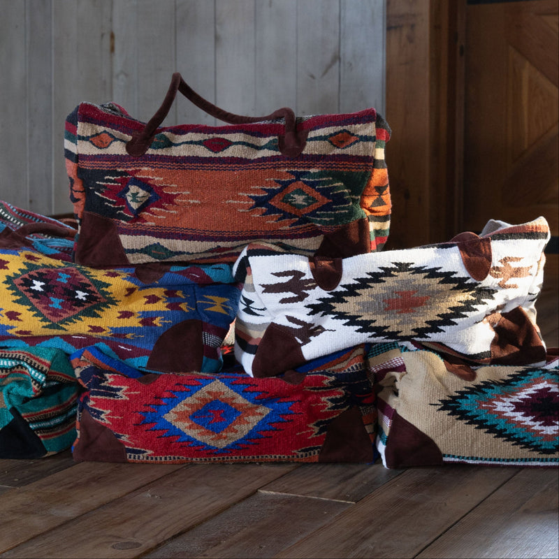 Stack of Weekender Bags All Colors on a wooden floor with a rustic wooden wall in the background.