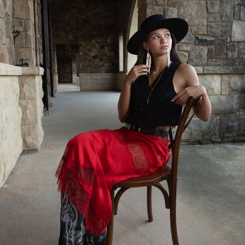 Woman wearing a black hat and black dress with Divine Goddess White Beaded earrings, standing against a stone wall.
