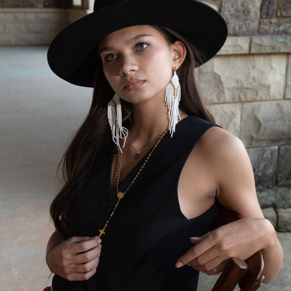 Woman wearing a black hat and red skirt with Magical Rosary Necklace long sitting on a wooden chair