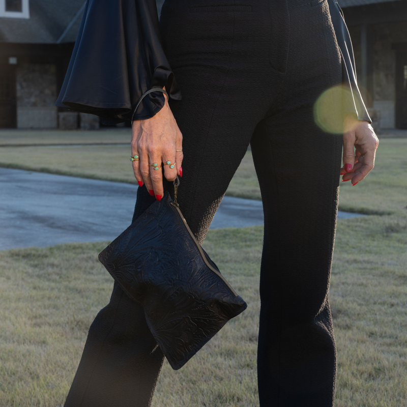 Good Tidings Styke Black leather wallet, One World Traveler Clutch, with intricate embossed design held by woman