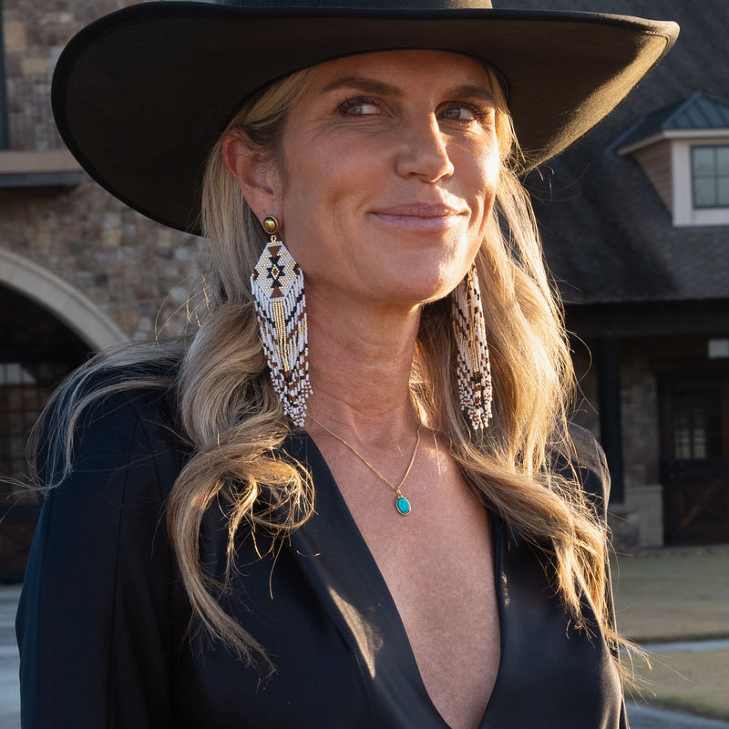 Woman wearing a black hat and tribal beaded earrings, and the Sacred Sky Pendant Necklace  with a building in the background