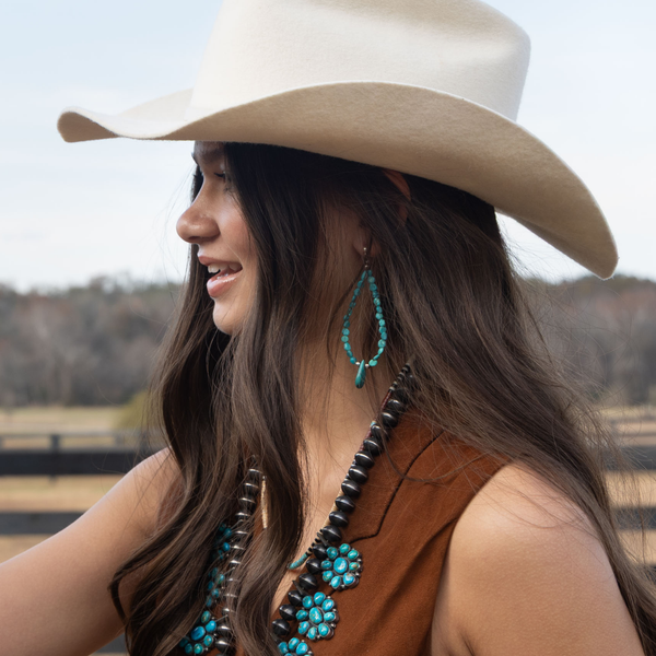 Woman wearing a beige cowboy hat and tears of turquoise earrings and jewelry outdoors